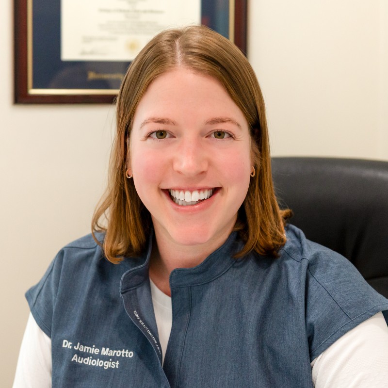 Dr. Jamie Marotto, audiologist, smiling in a blue clinic vest over a white shirt